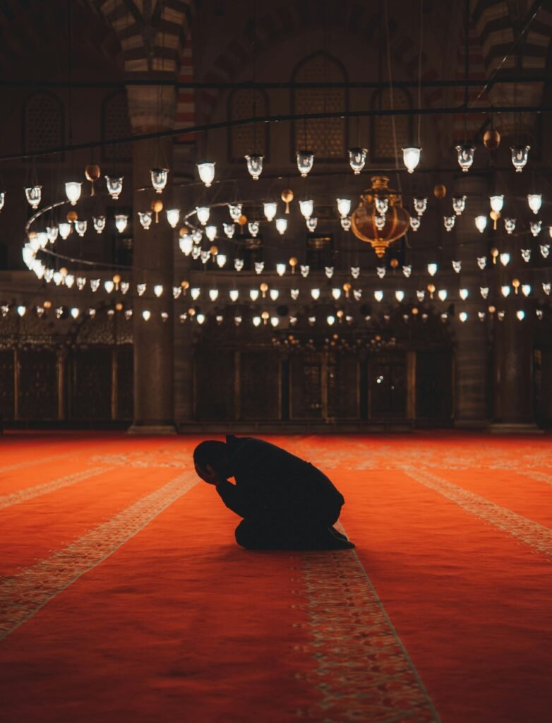 A man in silhouette kneels in prayer inside a beautifully illuminated mosque in Istanbul.