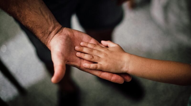 Close-up of a child's hand resting gently on a man's hand, symbolizing love and support.