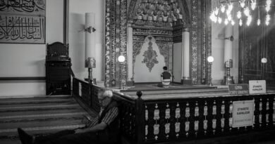 Black and white capture of a mosque interior with individuals engaged in prayer and reflection.