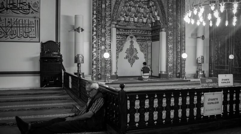 Black and white capture of a mosque interior with individuals engaged in prayer and reflection.