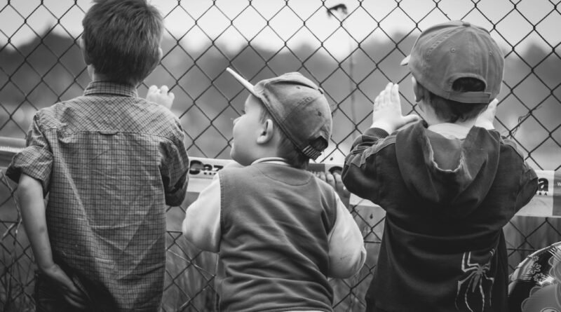 Black and white image of three young boys peering through a chain-link fence.