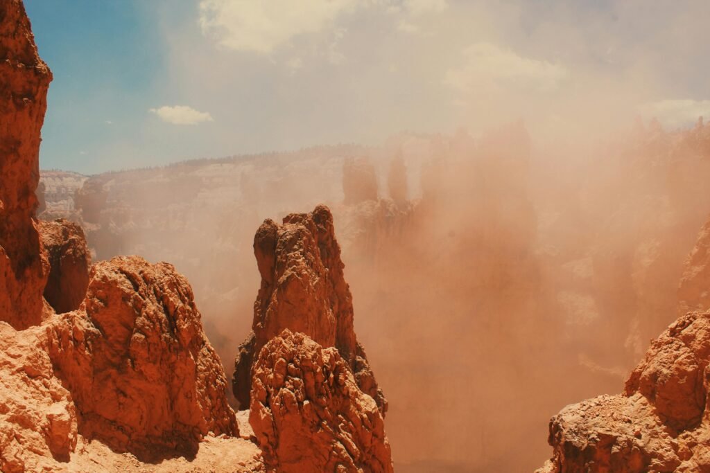 Stunning view of rocky sandstone cliffs enveloped in a desert sandstorm under clear blue skies.
